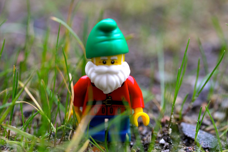 a lego man walking in grass with a white beard and green stocking hat