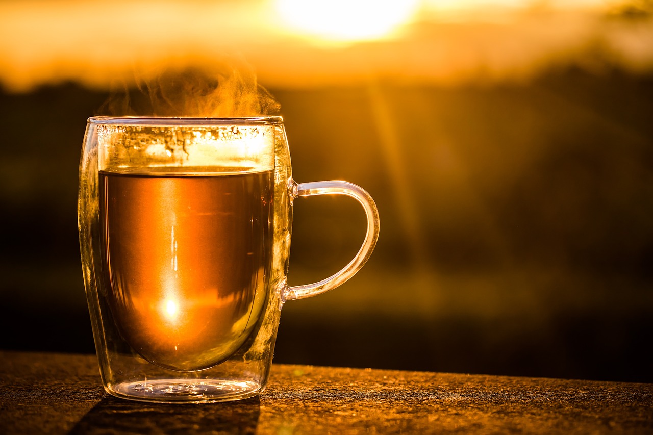 Tea in a clear cup with a sunset in the background.